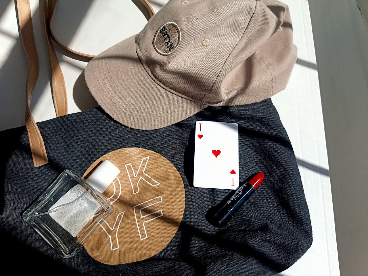 gallery-02 Stylish flat lay featuring cap, tote bag, red lipstick, perfume, and playing card, emphasizing lifestyle.